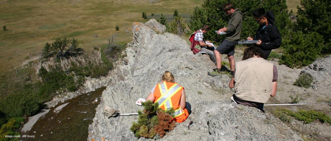 Student wearing reflective vest and other students atop a rocky outcropping.