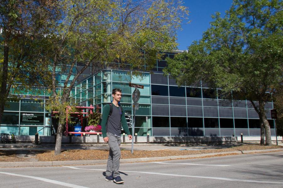 A student crosses the street in front of the Wallace building, home of the Clayton H. Riddell Faculty of Environment, Earth and Resources.