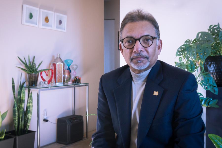 Dr. C. Emdad Haque standing indoors in a suit by a table.