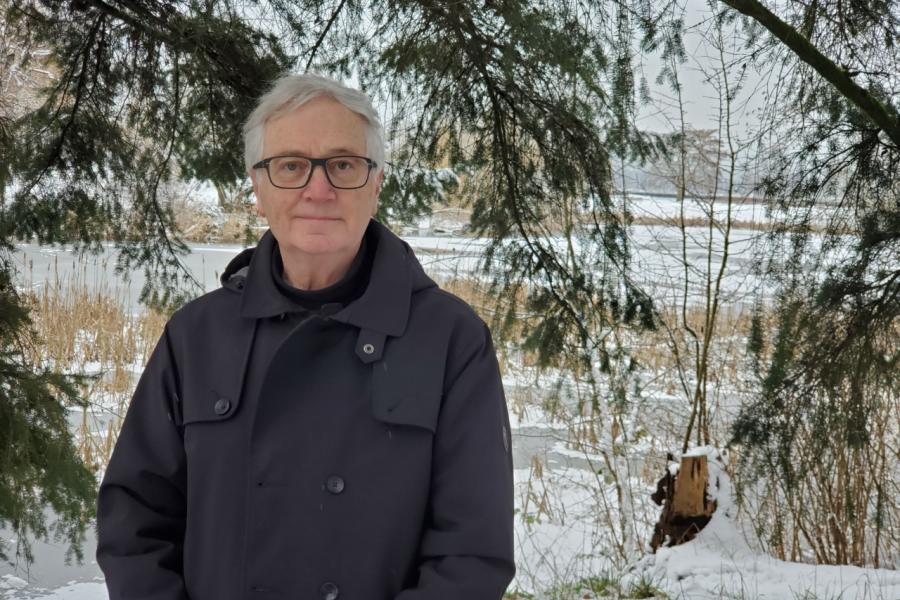 Doctor ronald stewart posing outside in a black jacket near some trees.