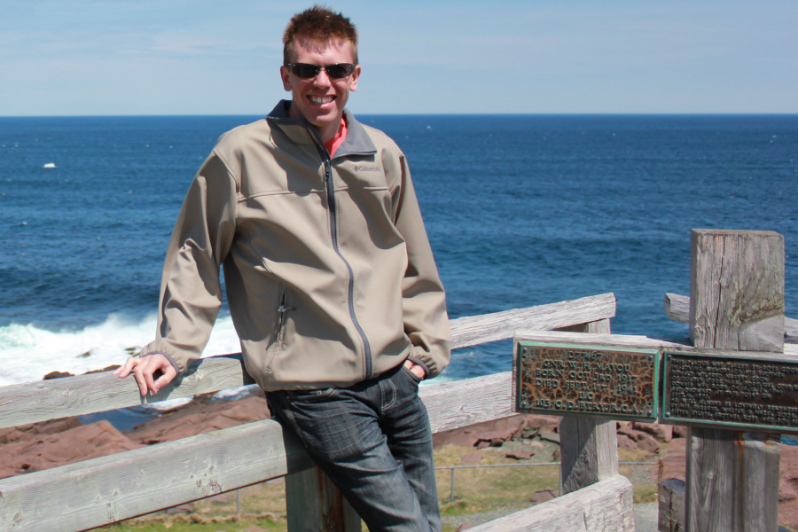 Doctor russel hiebert in brown jacket leaning against a fence outside.