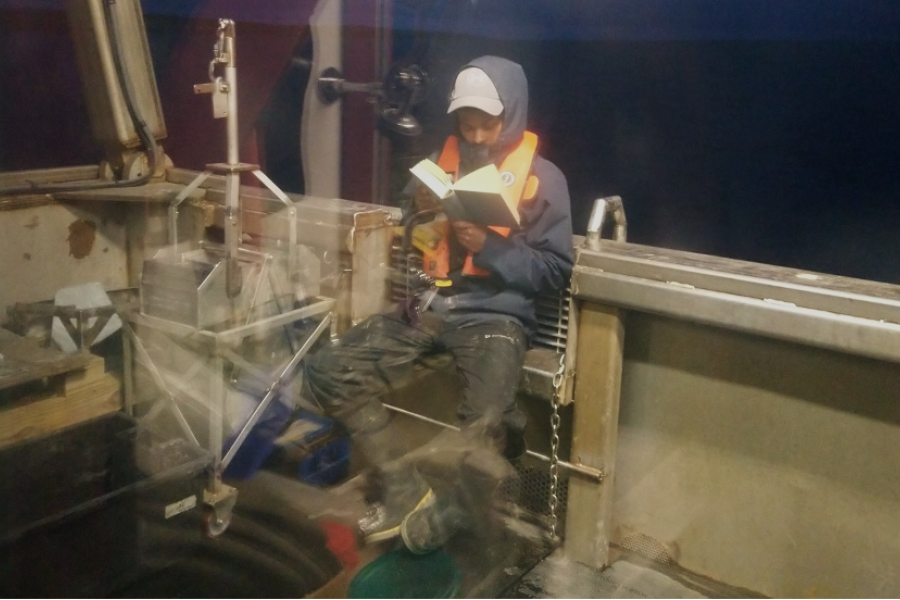 Durell Desmond sits reading a book bundled up on a research vessel