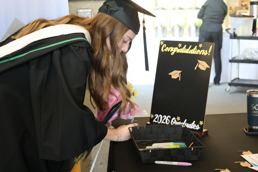 Graduate in cap and gown signs name on display