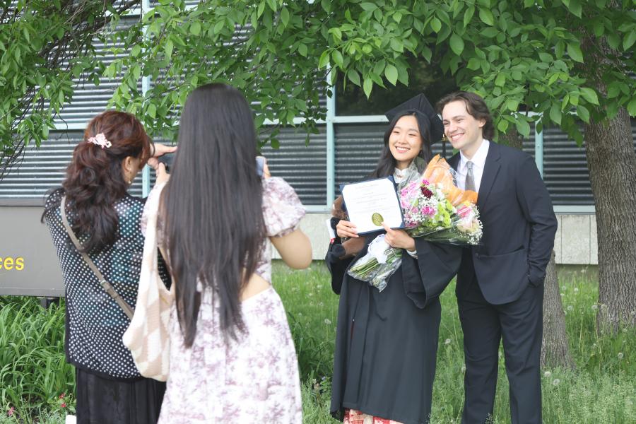 Graduate and guest, flowers, and parchment outside the Wallace building.
