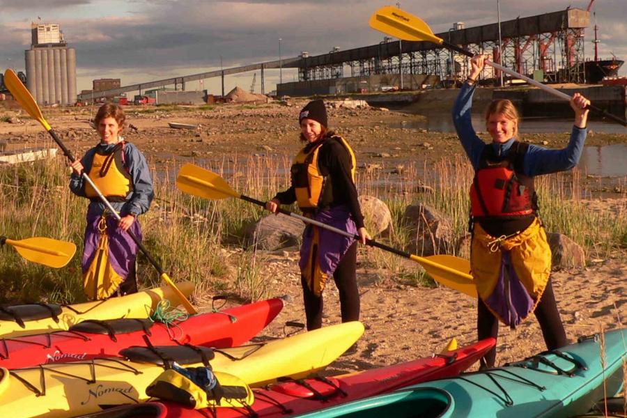 People standing next to kayaks holding paddles. 