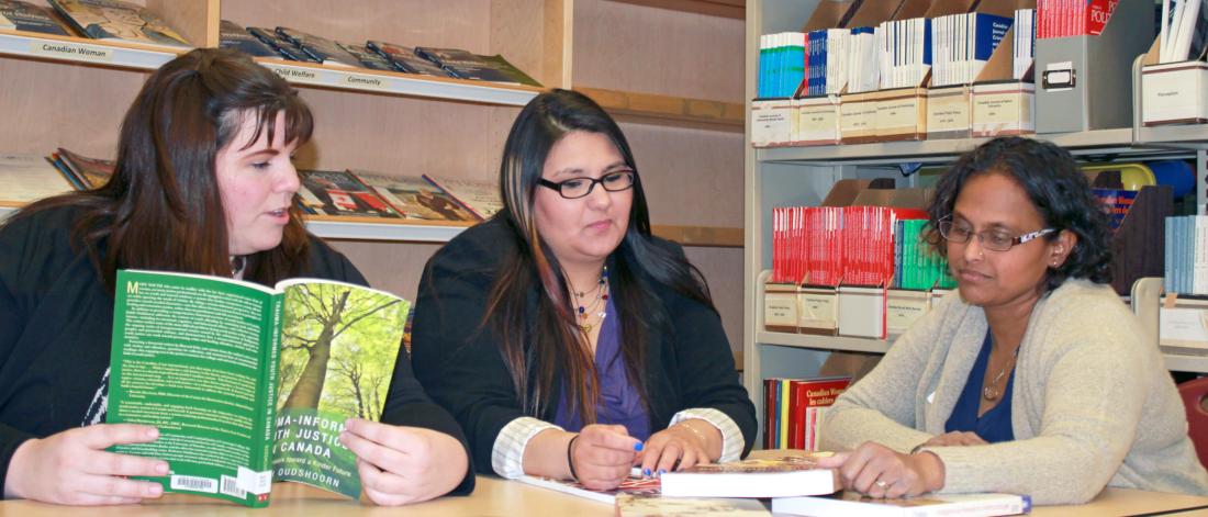 Three inner city social work students work together at a desk in a library.