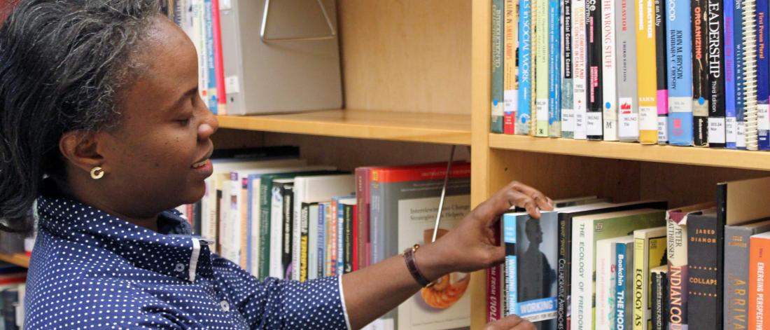 A woman stands at a bookshelf looking through the books.