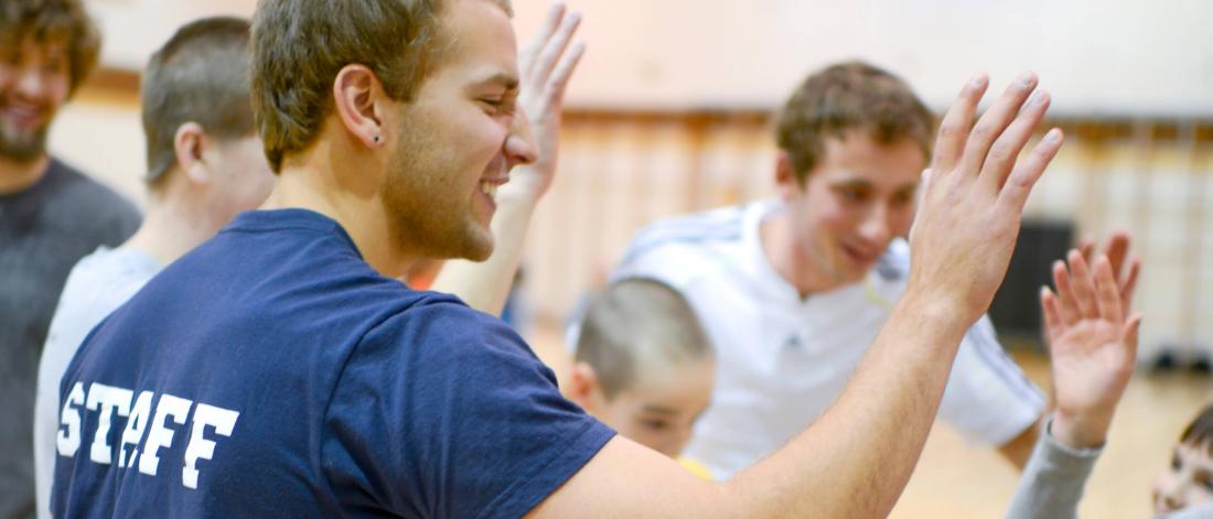 Bachelor of physical education students high five a class of young students they are teaching in a gymnasium.