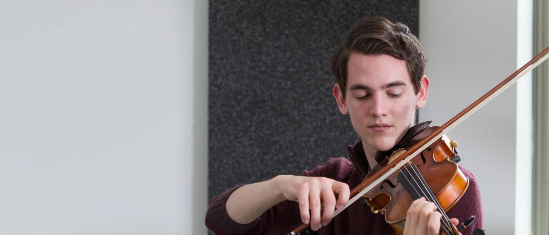 A music minor student practices the violin in a practice room.