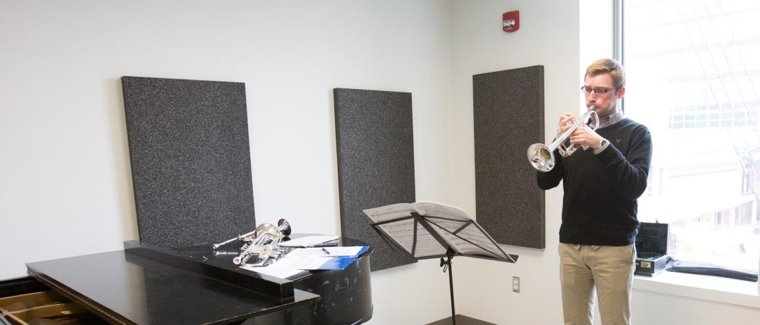 A Music minor student practices an instrument in a large room with a window and piano.