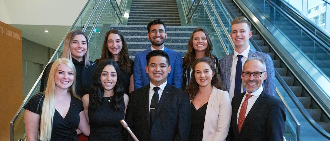 A group of nine Asper students stand together with a community member.