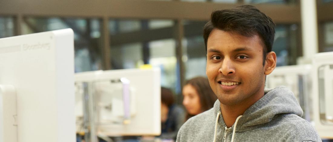 A student is smiling while seated at a desktop computer work station.