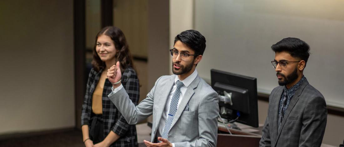 Three Asper School of Business students stand together giving a presentation at the front of a classroom.