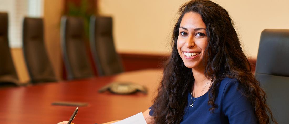 A student sits at a boardroom table smiling.