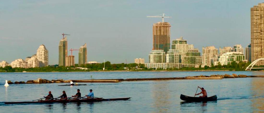 Two groups of people paddling canoes on a lake with a cityscape behind them.