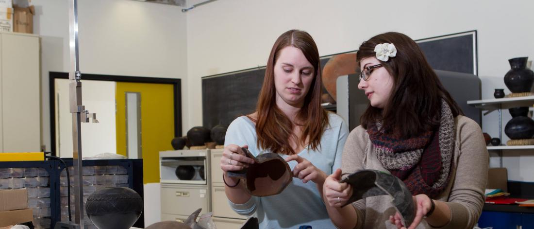 Two anthropology students hold artifacts.