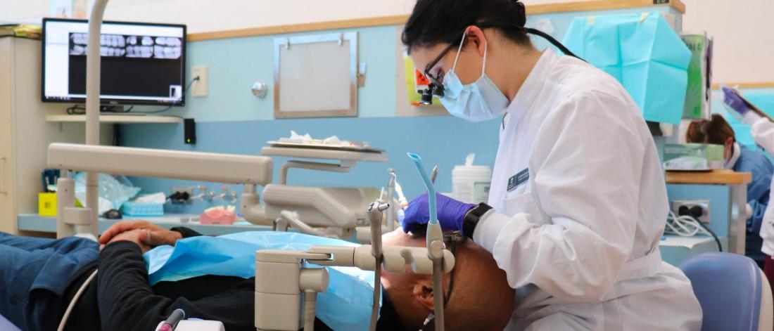 a dental hygienest performs an oral exam on a patient.