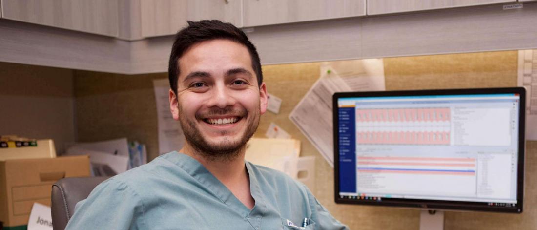 A dentistry student smiles while seated at a desk.