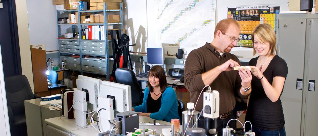 Two geology students work with a professor. 