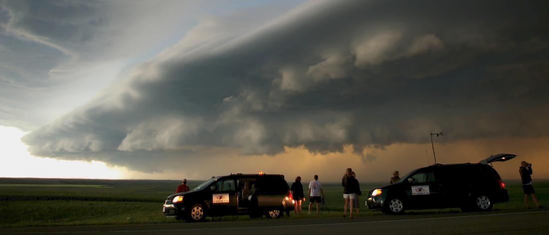 Students watch a large storm forming over a field.