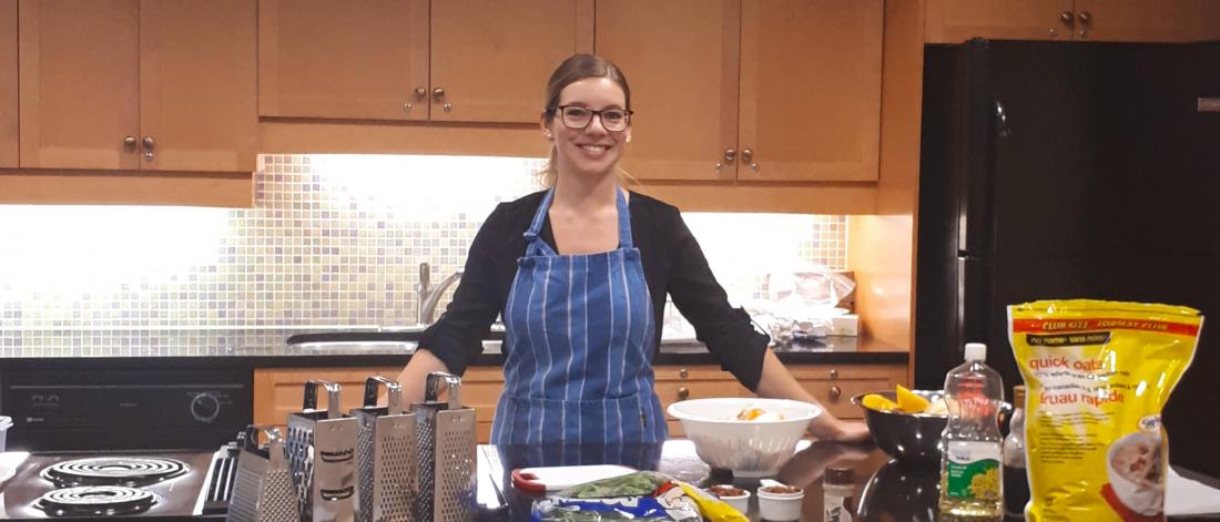 A human nutritional scientist stands at a kitchen counter with various food items spread out in front of her.