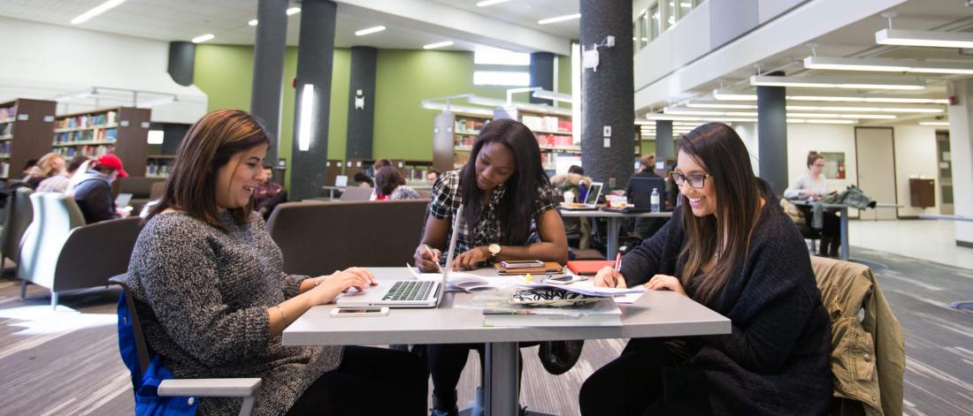 Three students seated at a table studying in a library.