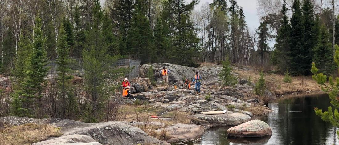 Students work in a scenic outdoor forested area near a body of water.