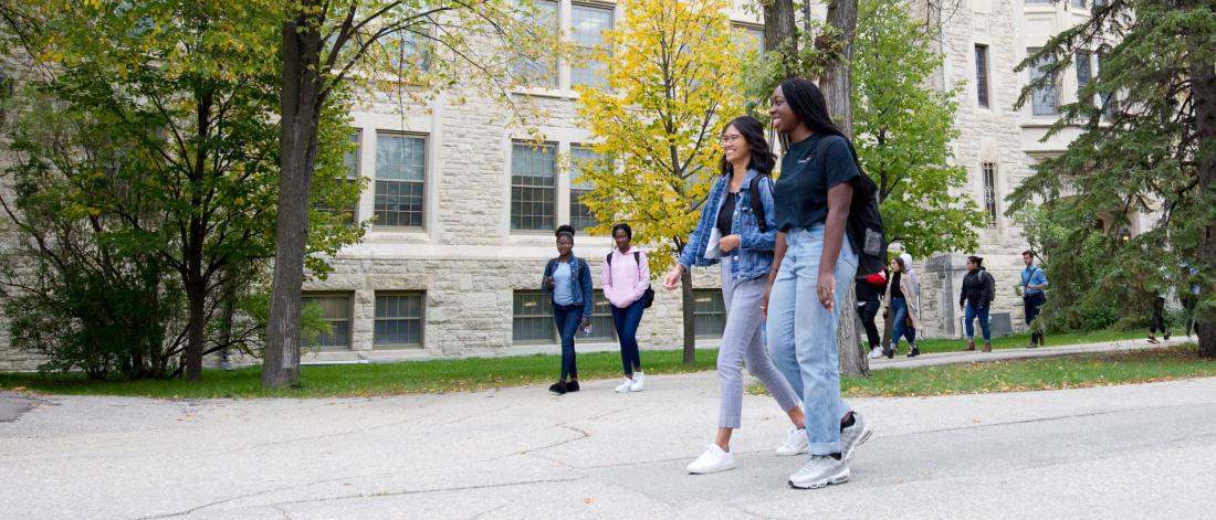 Students walking in pairs in front of the Tache Arts building at the University of Manitoba.