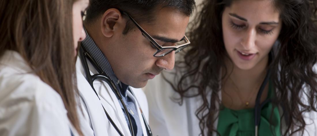 Close-up of three young medicine students in white coats look down at something out of frame