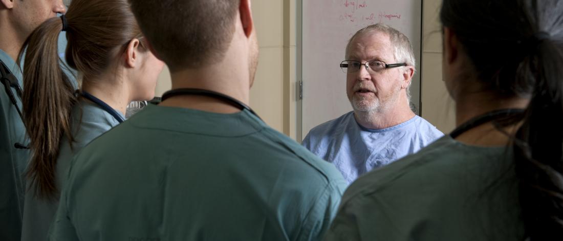 An instructor speaks to a group of four medicine students dressed in scrubs