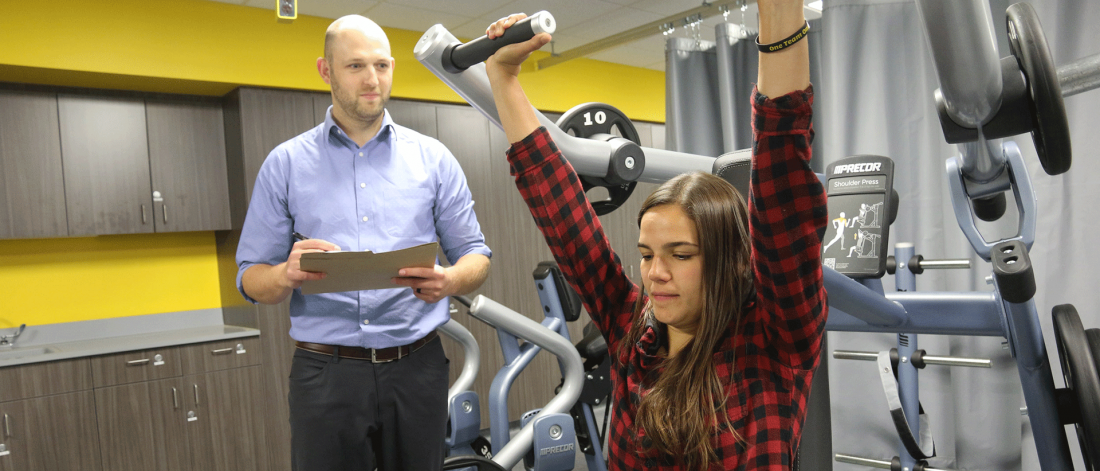 A clinician assesses a patient who is using a shoulder press.