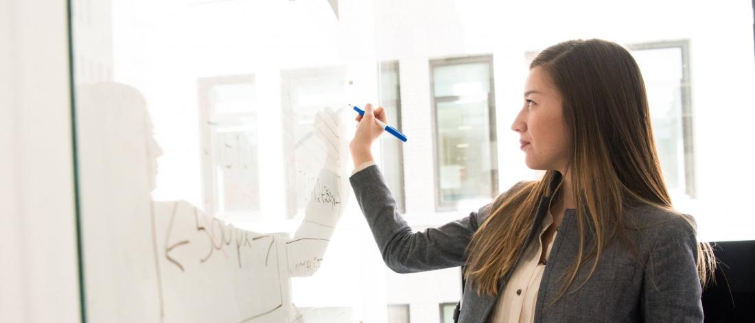 A woman stands while writing on a whiteboard.