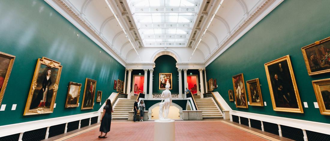 Interior photo of people enjoying paintings on dark green walls of the National Gallery of Ireland in Dublin.