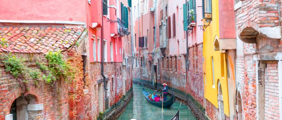 Gondola on narrow canal lined by pink buildings.