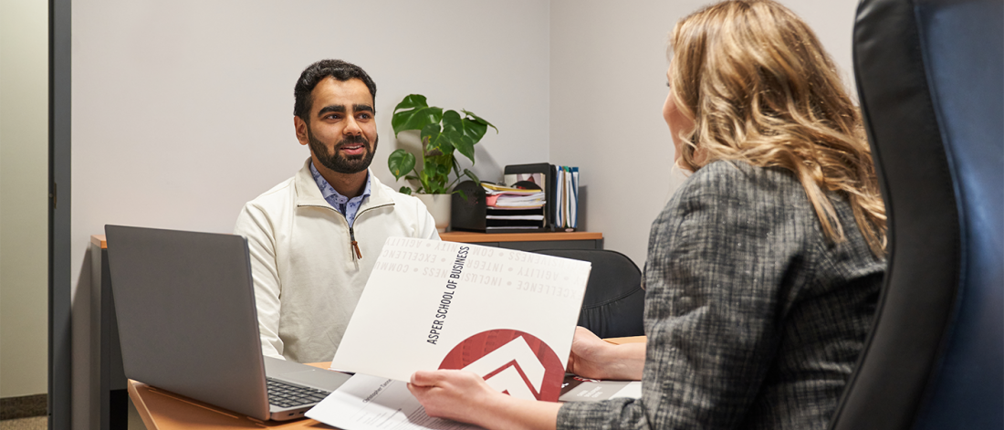 Asper student sitting at desk with staff member talking.