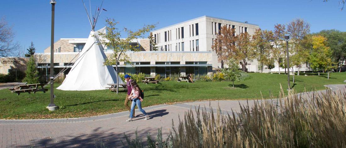 Two students walking on campus in front of a teepee.