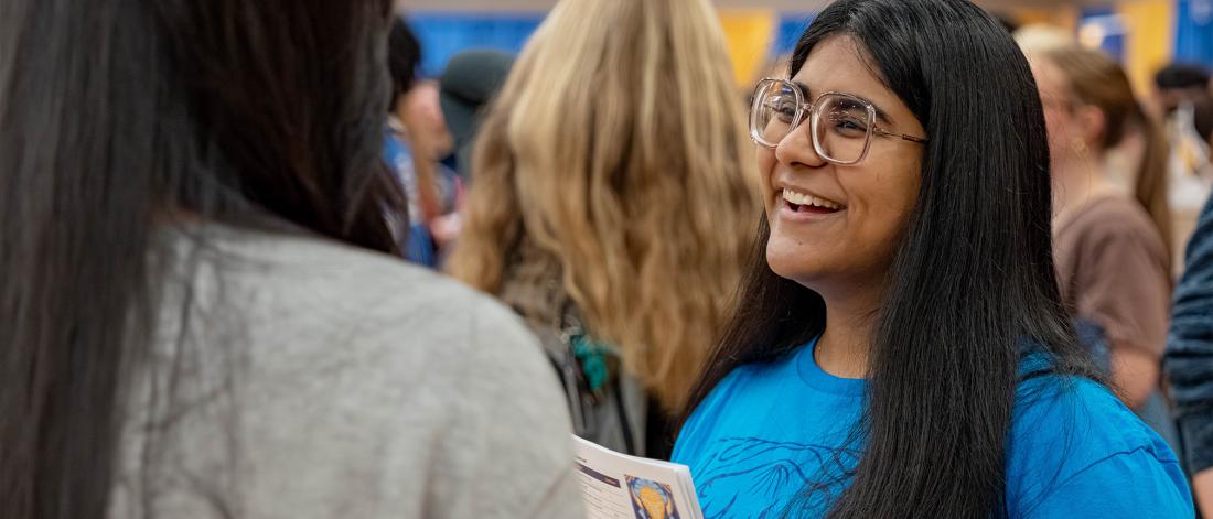 A student wearing a Faculty of Arts t-shirt is speaking to a prospective high school student. 