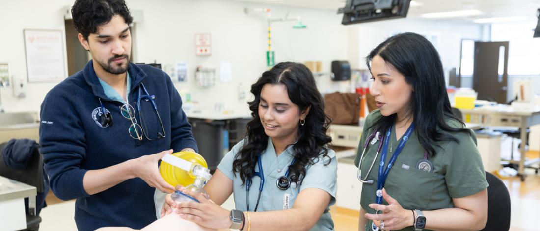 Close-up of two medicine students and an instructor intubating a simulation manikin.