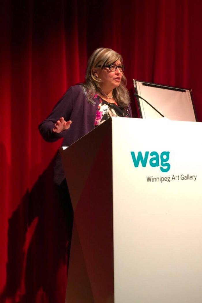 Art History graduate Diane Lafournaise stands at a podium speaking at the Winnipeg Art Gallery.