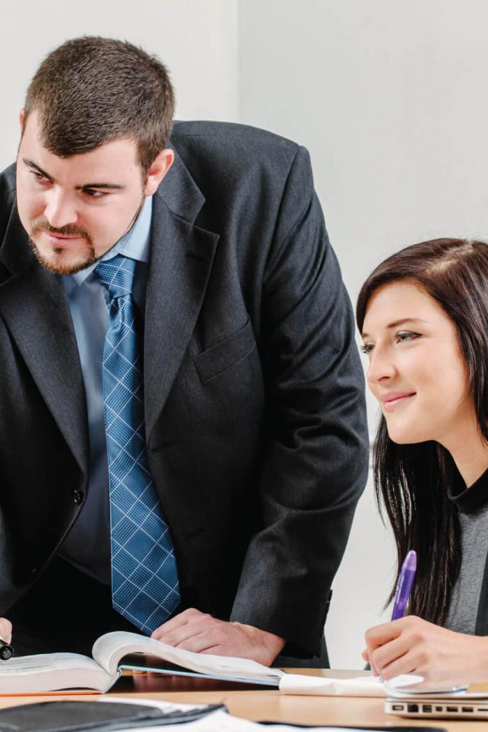 Two well dressed Asper students take notes in a boardroom setting.