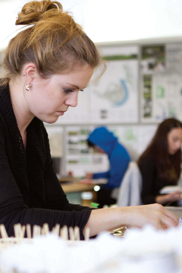 An architecture student carefully works on a project at her desk.