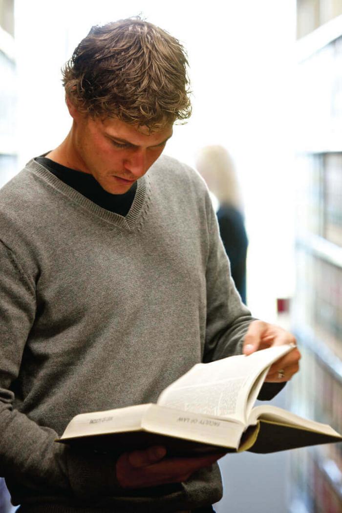 A law student skimming a book in an isle within the library stacks.