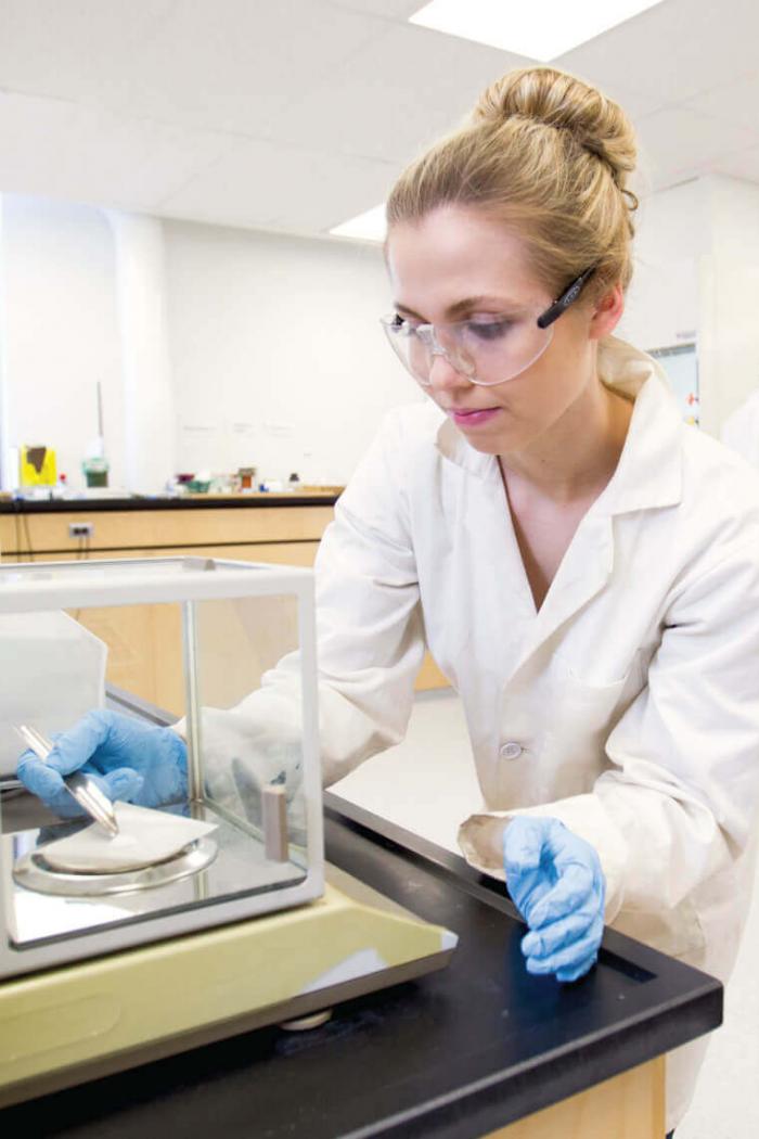 A science student dressed in protective wear inspecting a cultured substance inside an incubator.