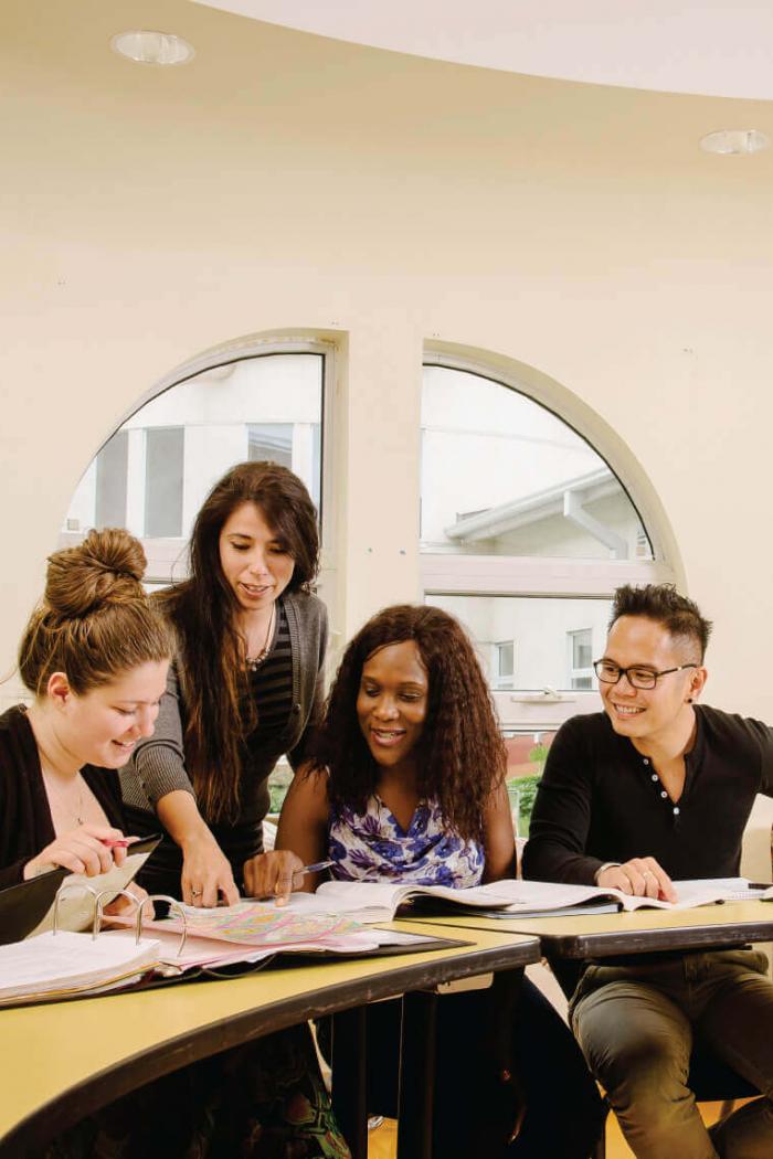 A group of studying social work students pointing out something specific in one of their notebooks.