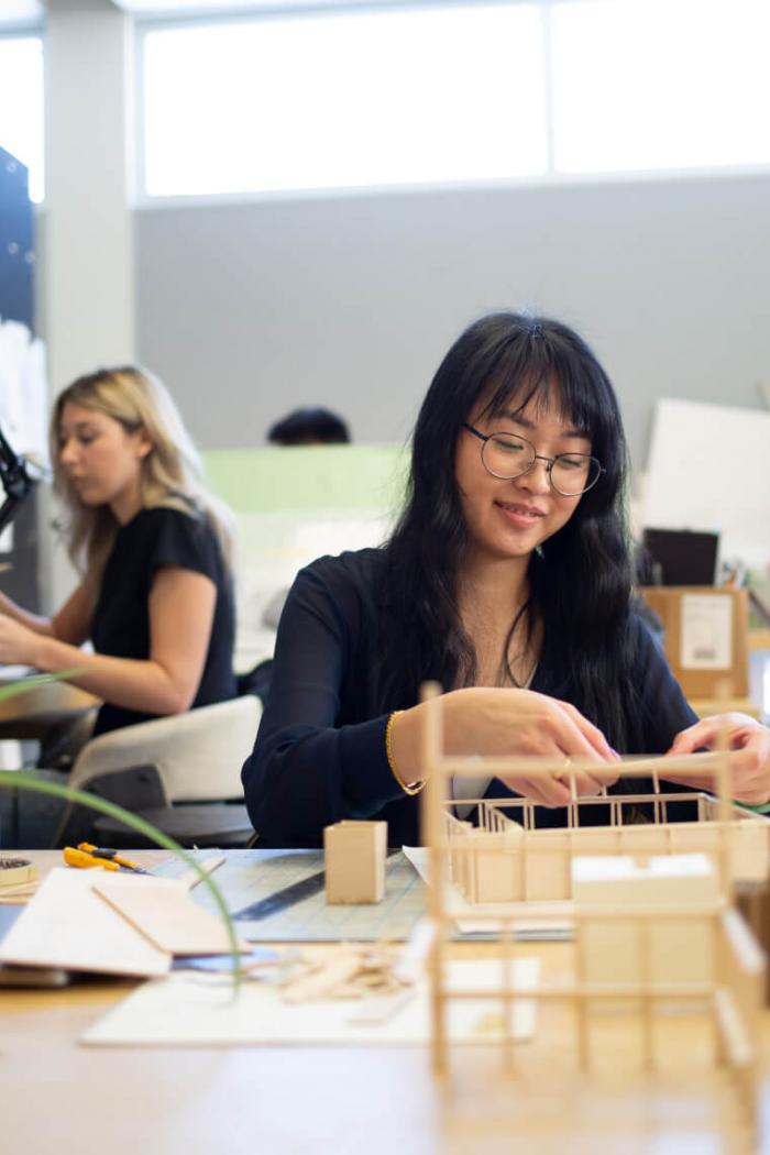 An architecture student carefully works on a project at her desk.