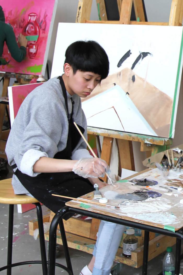 A Faculty of Arts student sits in front of a canvas working on a painting.