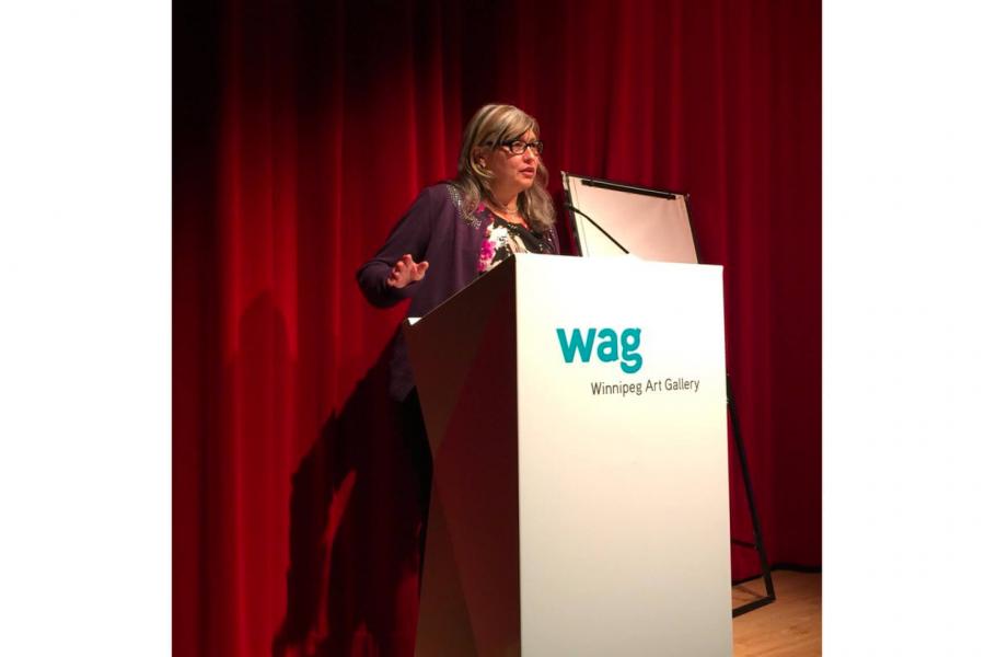 Art History graduate Diane Lafournaise stands at a podium speaking at the Winnipeg Art Gallery.