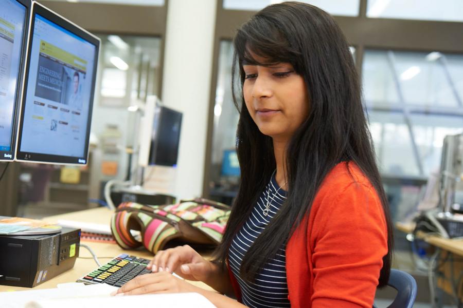 A student works at a computer with a binder in front of her.