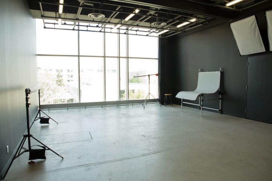 The lighting studio with a large window, blackout curtains, black walls and various pieces of photography equipment.