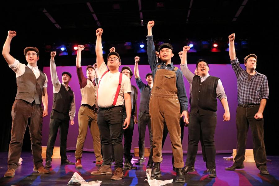 A group of students stand on stage with a purple background during a men's musical theatre ensemble performance.